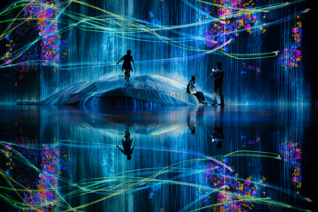 Visitors surrounded by colorful projected light and reflections at teamLab Borderless