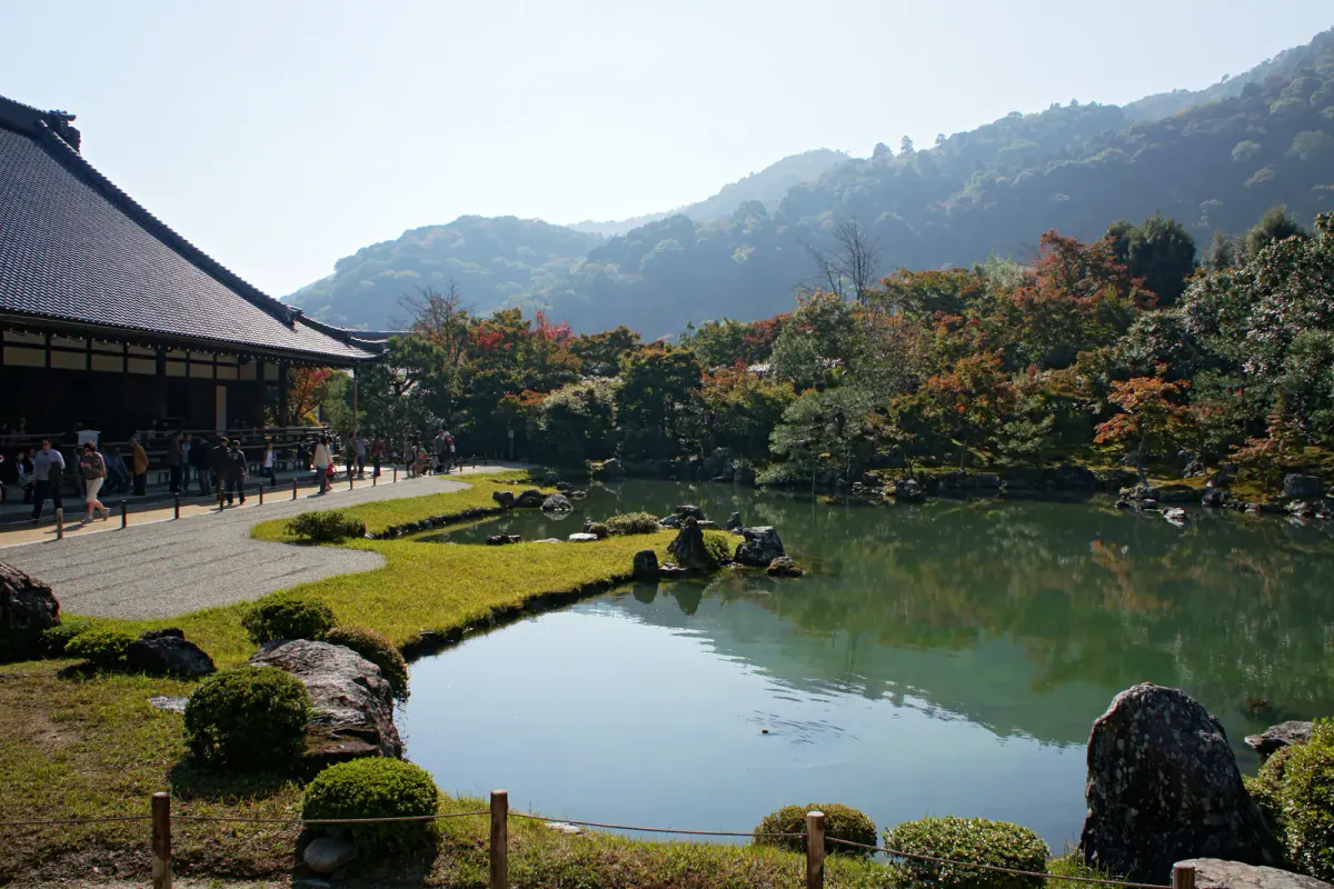 Tenryu-ji's pond garden in Arashiyama, with temple buildings, wooded hills and trees showing mixed green and autumn tones